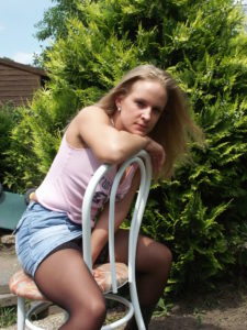 Blonde im Unterhemd sitzt auf Stuhl im Garten